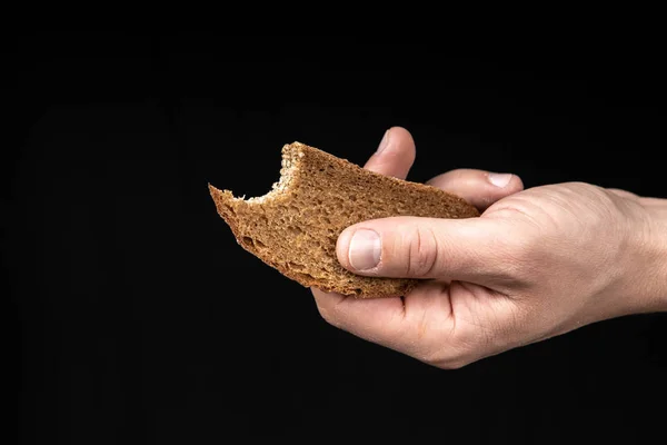 Man holds a bitten bread in his hand on black background — Stock Photo, Image