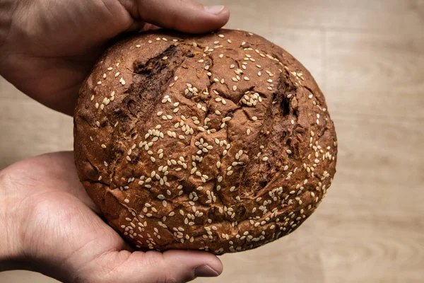 Man 's handen houden lekker vers brood van donker brood met sesamzaad op lichte achtergrond — Stockfoto