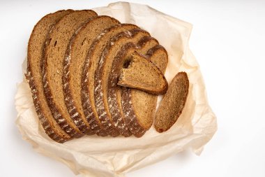 Çavdar ekmeği beyaz arka planda, ekmek kağıdının üzerinde parçalanmış olarak duruyor.