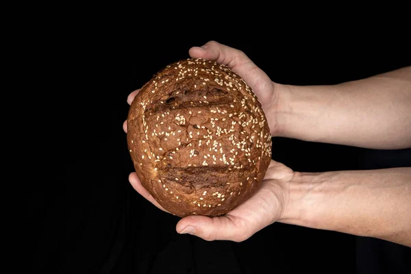 Man 's handen houden lekker vers brood met sesamzaad op zwarte achtergrond — Stockfoto