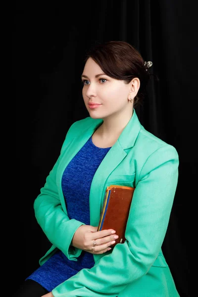 Зніміть портрет дівчини зі слов'янського вигляду, одягненої в блакитну блузку і синьо-зелену куртку на чорному тлі з коричневим записником в руках. — стокове фото