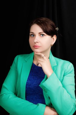 Studio  close up portrait of a girl of Slavic appearance worn a blue blouse and a blue-green jacket on a black background