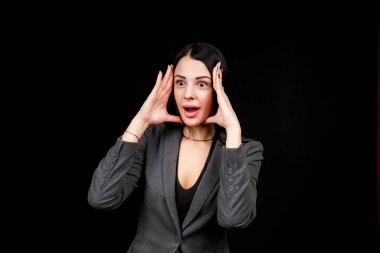 Young woman is angry. The girl wear casual grey jacket on a black background. Evil woman, hands on her sides