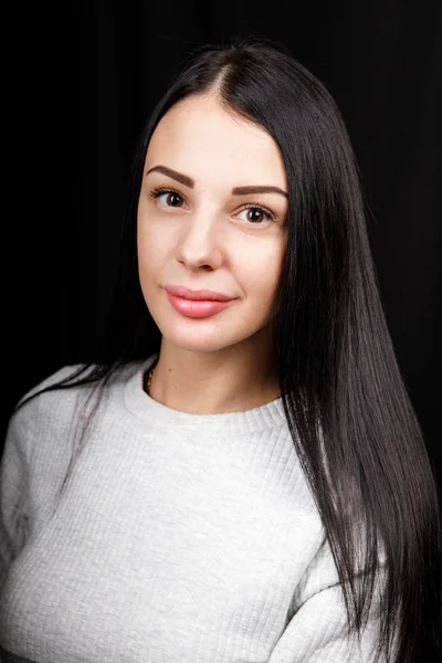 Portrait of serious beautiful female with black hair, has minimal makeup, looks calmly at camera, wears white jumper, stands against black background, being deep in thoughts — 스톡 사진