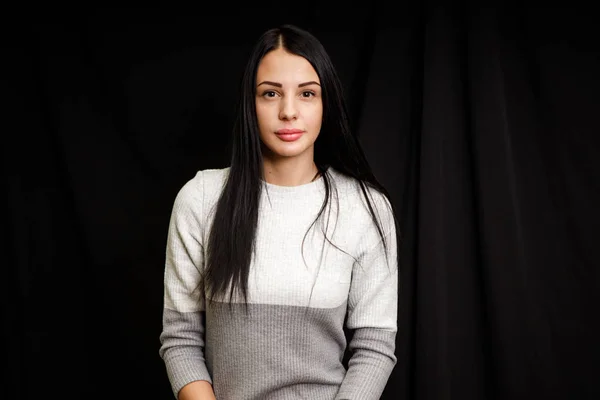 Retrato de mujer hermosa seria con el pelo negro, tiene un maquillaje mínimo, mira con calma a la cámara, usa jersey blanco, se levanta contra el fondo negro, siendo profundo en los pensamientos — Foto de Stock