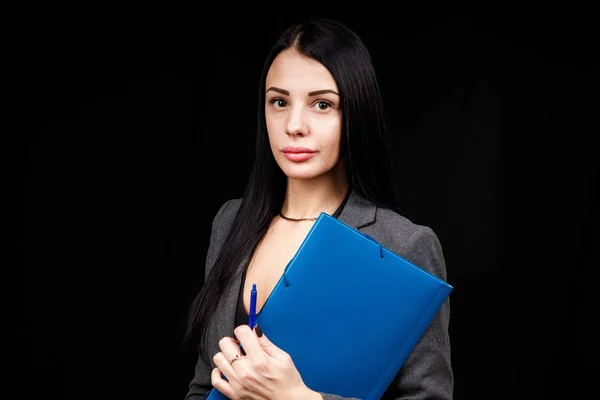 Задумчивая привлекательная молодая женщина в серой куртке, держащая синюю папку и думая на черном фоне — стоковое фото