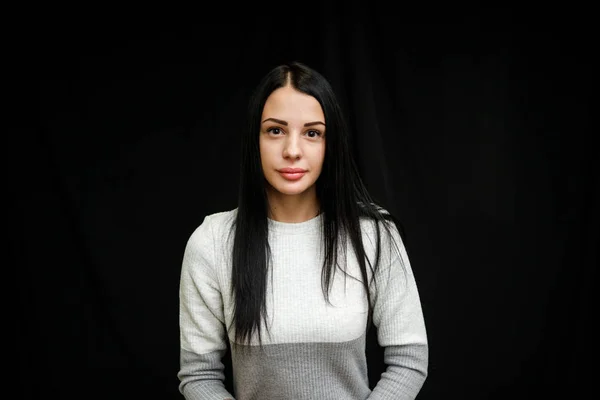 Retrato de mulher bonita grave com cabelo preto, tem maquiagem mínima, olha calmamente para a câmera, usa saltador branco, fica contra o fundo preto, sendo profundo nos pensamentos — Fotografia de Stock