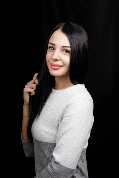 Portrait of serious beautiful female with black hair, has minimal makeup, looks calmly at camera, wears white jumper, stands against black background, being deep in thoughts — Stok fotoğraf