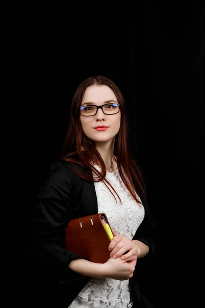 Studio close-up portret van een meisje van Slavische verschijning gedragen zwarte jas op een zwarte achtergrond met bruine notebook in haar handen — Stockfoto