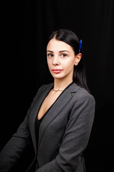 Retrato de jovem mulher de negócios em uma jaqueta cinza no fundo preto com caneta atrás da orelha — Fotografia de Stock