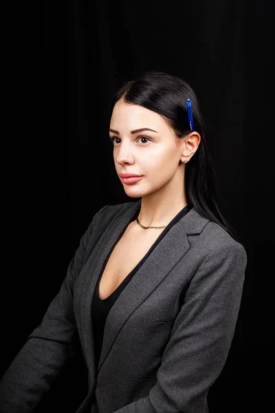 Портрет молодой деловой женщины в серой куртке на черном фоне с ручкой за ухом — стоковое фото