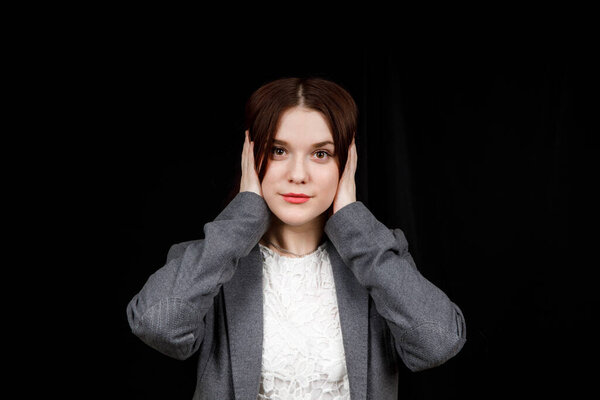 Confused woman holding hands on head over black studio background. Portrait of young serious girl closing her ears, hear no evil, deafness concept, copy space