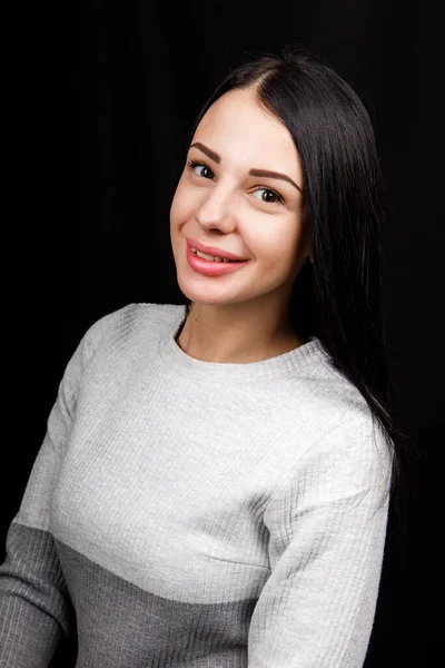 Portrait of serious beautiful female with black hair, has minimal makeup, looks calmly at camera, wears white jumper, stands against black background, being deep in thoughts — 스톡 사진