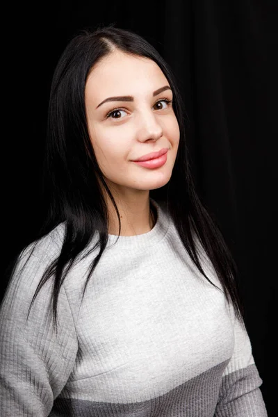 Portrait of serious beautiful female with black hair, has minimal makeup, looks calmly at camera, wears white jumper, stands against black background, being deep in thoughts — 스톡 사진