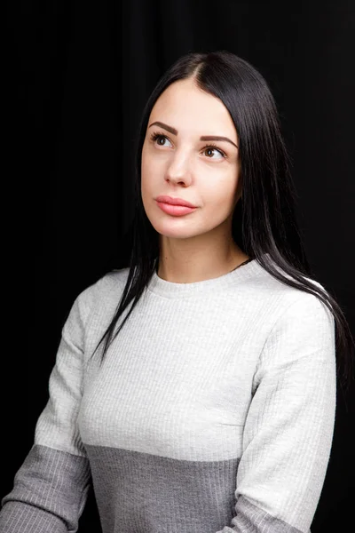 Porträt einer ernsthaften schönen Frau mit schwarzem Haar, minimalistisch geschminkt, blickt ruhig in die Kamera, trägt weißen Pullover, steht vor schwarzem Hintergrund, ist tief in Gedanken — Stockfoto