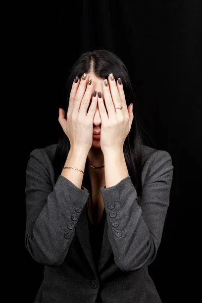 See no evil concept. Portrait of a young scared woman covering eyes with hands, standing on dark studio background. Mixed girl close the eyes with palms while ignoring something