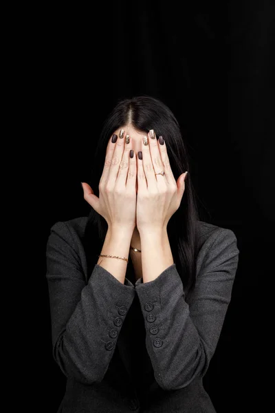 See no evil concept. Portrait of a young scared woman covering eyes with hands, standing on dark studio background. Mixed girl close the eyes with palms while ignoring something