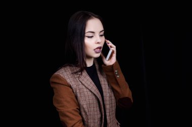 Neşeli ve başarılı genç kadın moda blogcusu telefonda duygusal olarak konuşuyor. Gri ceketli güzel bir kadın elinde akıllı telefon tutuyor.