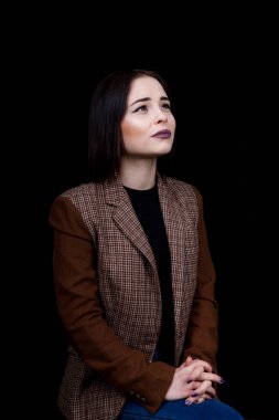 Sıradan giyinmiş sevimli mütevazı kız siyah arka planda gülümsüyor.