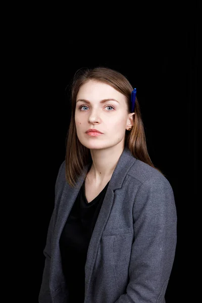 Retrato de una joven mujer de negocios con una chaqueta gris sobre fondo negro con bolígrafo detrás de la oreja — Foto de Stock