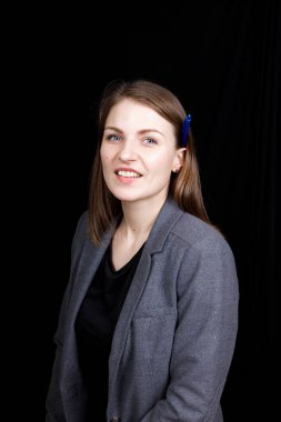 Siyah arka planda gri ceketli, kulağının arkasında kalem olan genç bir iş kadını portresi.