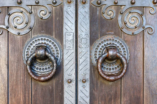 Entrada texturizada de madera marrón envejecida con tiradores de puerta de anillos y detalles de metal. Fondo de arquitectura. Puerta de madera vieja con remaches y manija de puerta de metal envejecido en forma de anillo —  Fotos de Stock