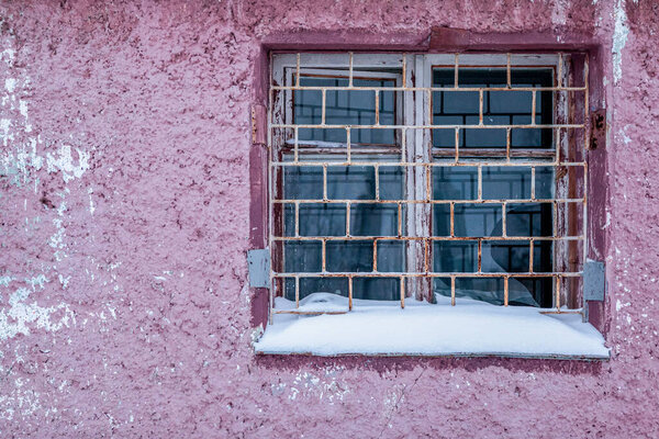 Window with iron grating in a wall of old pink concrete building