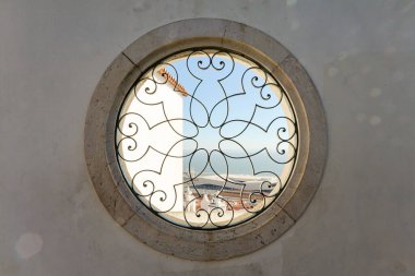 Siyah metal çitli yuvarlak bir pencere ve gökyüzü manzaralı eski bir taş cephede bir desen.
