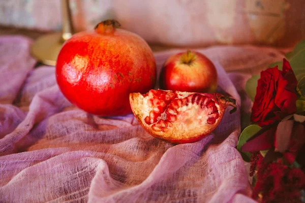 Whole and broken into pieces pomegranates are laid out on a pink fabric served with an apple on a rustic table — Stock Photo, Image