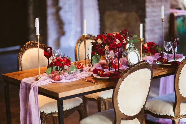 Flowers bouquet of pink, red and white roses in the vase, plate with pomegranates, beautiful candles and invitation cards on the wedding table covered with pink tablecloth — Stock Photo, Image