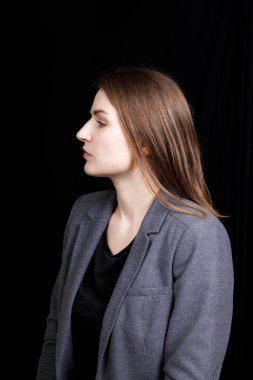 Gri iş ceketli, beyaz tenli hoş bir kadın siyah arka planda profil oluşturdu.