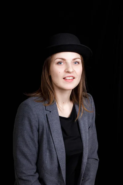 Милая молодая девушка в шляпе и серой куртке на черном фоне — стоковое фото