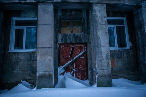 Okna i drzwi wybite deskami na szarym budynku pokrytym śniegiem — Zdjęcie stockowe