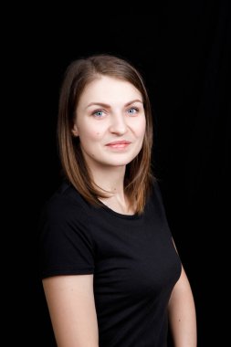 Siyah tişörtlü genç bir kadın siyah arka plandaki kameraya bakıyor.