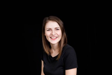 Siyah tişörtlü genç bir kadın siyah arka plandaki kameraya bakıyor.