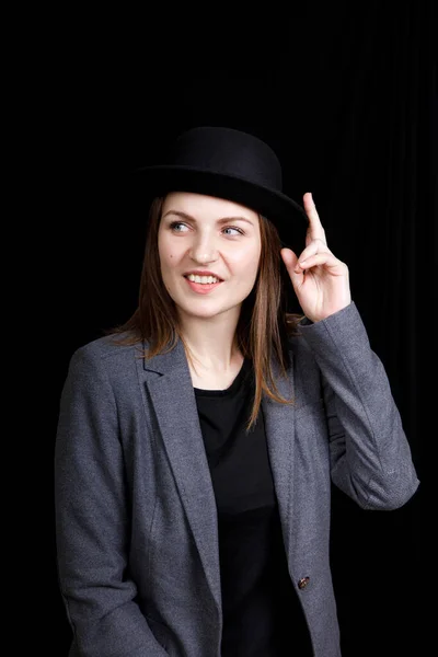 Niedliches junges Mädchen mit Hut und grauer Jacke auf schwarzem Hintergrund — Stockfoto