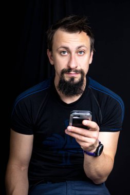 Karanlık bir geçmişi olan sakallı bir adam telefona bakar.