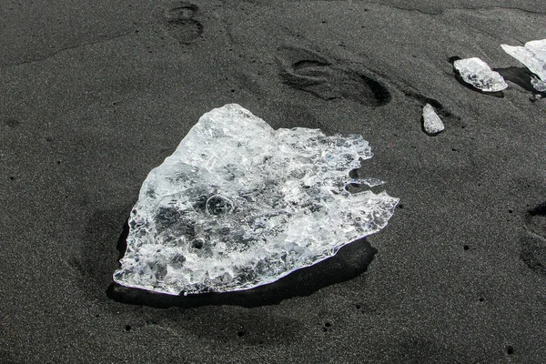 The block of ice is lying on the black volcanic sand on the \