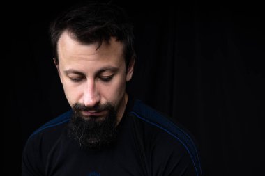 Koyu renk elbiseli, siyah arka planda sakallı genç bir adamın yakın plan portresi.