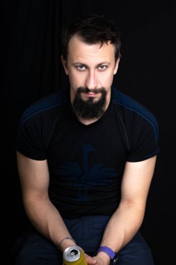 Genç bir adam bir elinde bira ve bir telefonuyla oturuyor.