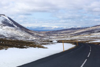 İzlanda 'da kış manzarasında yol. Yan tarafı karla kaplı asfalt yol.