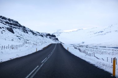 İzlanda 'da kış manzarasında yol. Yan tarafı karla kaplı asfalt yol.