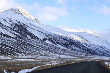 Karlı dağların yanındaki siyah yol. İzlanda Manzarası