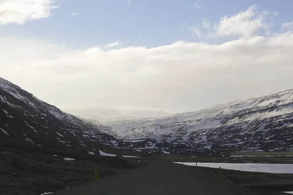 Тёмная асфальтовая дорога на фоне гор и океана. Экскурсия по Исландии. Геотермальная жара здесь — стоковое фото