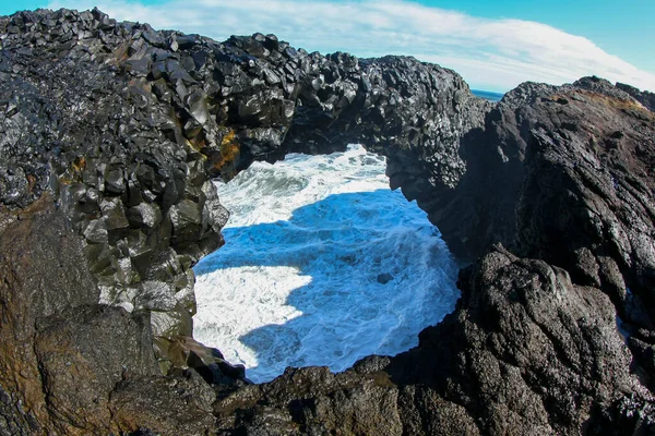 Океанская волна с пенными разломами на прибрежных скалах Исландии — стоковое фото