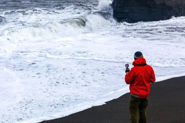 Muž v červené bundě fotografování vln na Atlantském oceánu na Islandu — Stock fotografie