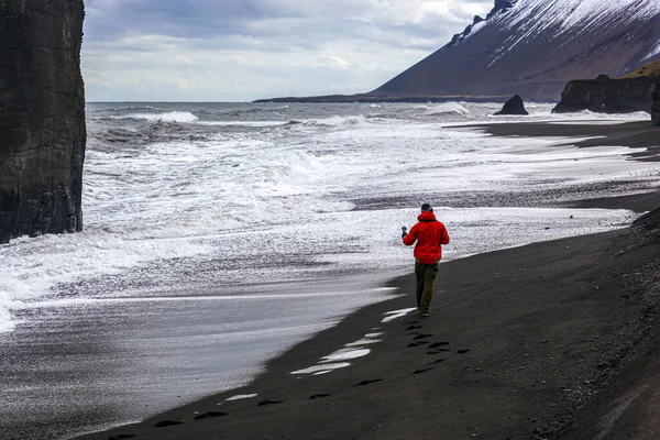 Человек в красной куртке фотографирует волны на Атлантическом океане в Исландии — стоковое фото