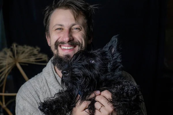 smiling man hugging his dog, a Scottish Terrier. Four-legged friend and his master