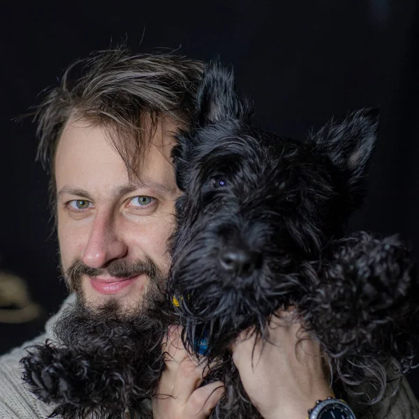 smiling man hugging his dog, a Scottish Terrier. Four-legged friend and his master