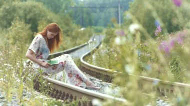 Kız tablet bilgisayar kullanıyor. Güzel kızıl saçlı kız ray üzerinde oturur ve bir tablet Pc sahiptir..